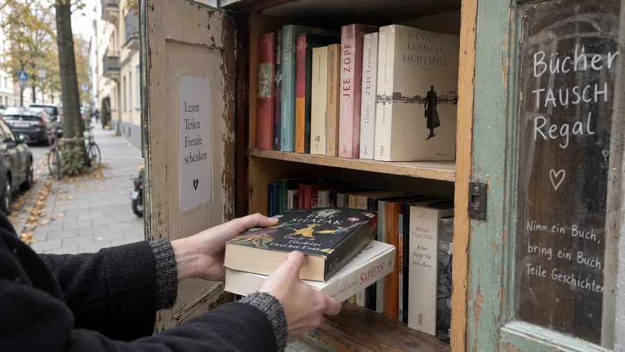 Bücher spenden statt wegwerfen: Hand stellt Taschenbücher in einen öffentlichen Bücherschrank auf der Straße, praktische Alternative beim Ausmisten von Büchern