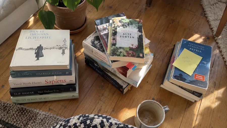 Bücher ausmisten vor dem Sortieren: drei Stapel Bücher auf Holzboden, einer davon mit Klebezettel markiert, praktischer Schritt beim Ausmisten vor dem Bücherregal ordnen