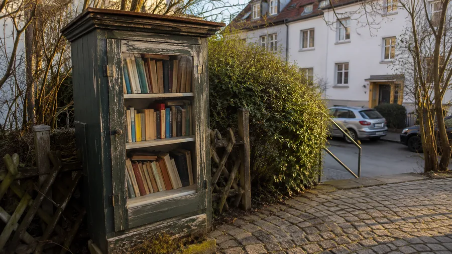 Öffentlicher Bücherschrank aus Holz mit leicht verwitterter Farbe, gefüllt mit Büchern, an einer Straße in der Nachbarschaft