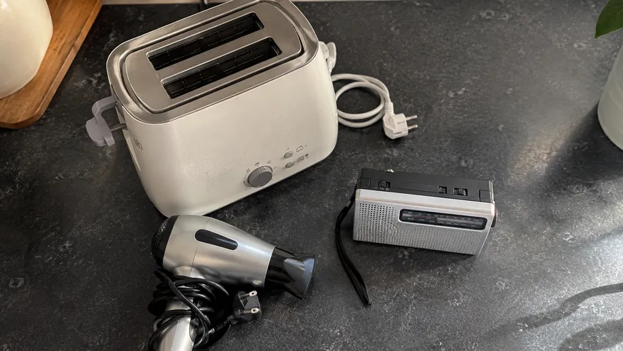 Küchenarbeitsplatte mit einem älteren, sauberen Toaster, einem Föhn mit aufgerolltem Kabel und einem kleinen Radio, zur Spende bereitgestellt