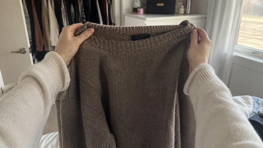 Nahaufnahme zweier Hände, die einen leicht getragenen Strickpullover auf Brusthöhe prüfend hochhalten