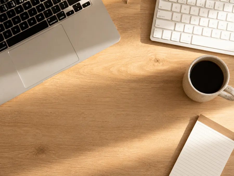 Minimalistische Schreibtischoberfläche von oben mit Laptop, Tastatur, Tasse und Notizblock im Homeoffice