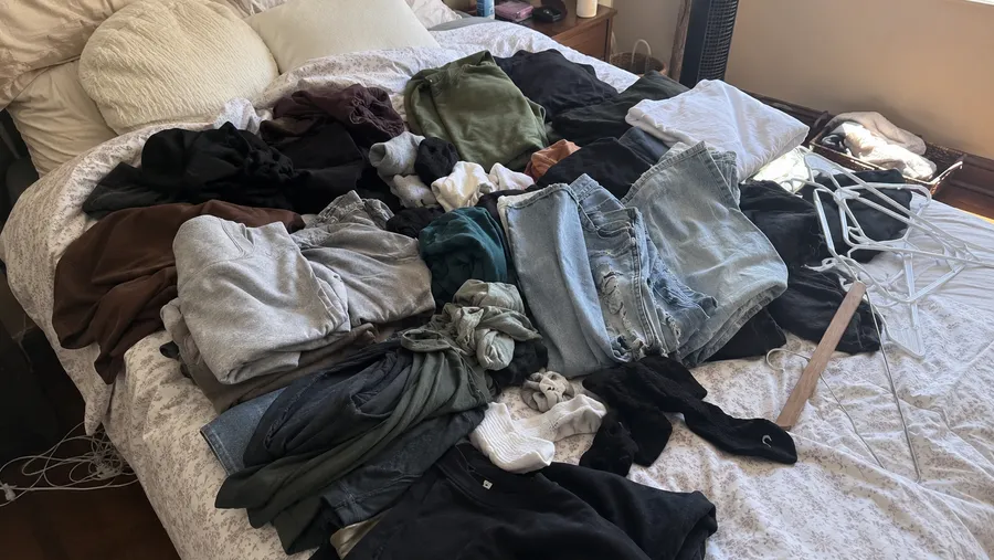 Draufsicht auf ein Bett, komplett bedeckt mit Kleidungsstücken aus dem Schrank, mitten im Sortierprozess