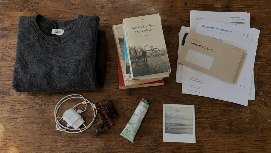 Flatlay auf einem Holztisch mit fünf getrennten Objektgruppen: Pullover, Bücher, Papiere, Alltagsgegenstände und ein Polaroidfoto