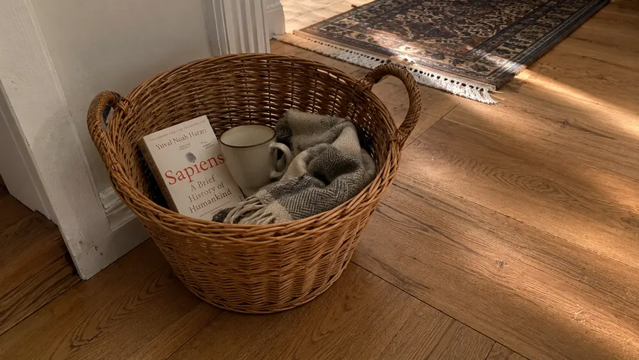 Ein Weidenkorb steht im Flur, teilweise gefüllt mit Alltagsgegenständen wie Buch, Tasse und Schal