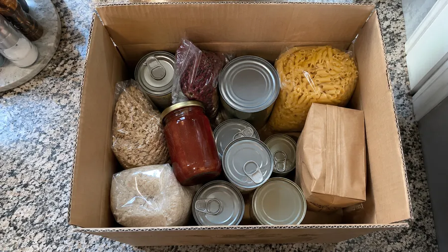 Pappkarton mit unverbrauchten, originalverpackten Konserven und Gläsern auf der Küchentheke