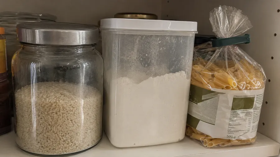 Glasbehälter mit Reis neben Kunststoffdose mit Mehl, daneben eine mit Clip verschlossene Nudelpackung in Originalverpackung