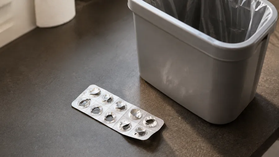 Leere Tablettenblisterverpackung neben einem kleinen Mülleimer, symbolisch für die getrennte Entsorgung von Verpackung und Medikamentenresten