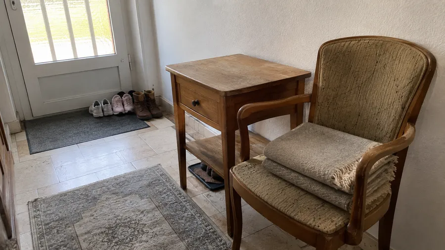 Kleiner Holzbeistelltisch und ein leicht abgenutzter Polsterstuhl in einem hellen Hausflur, bereit zur Abholung