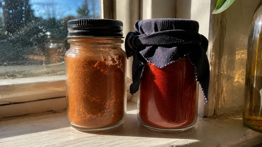 Nahaufnahme zweier Gläser Paprikapulver auf der Fensterbank, eines verblasst durch Sonnenlicht, eines kräftig rot und geschützt