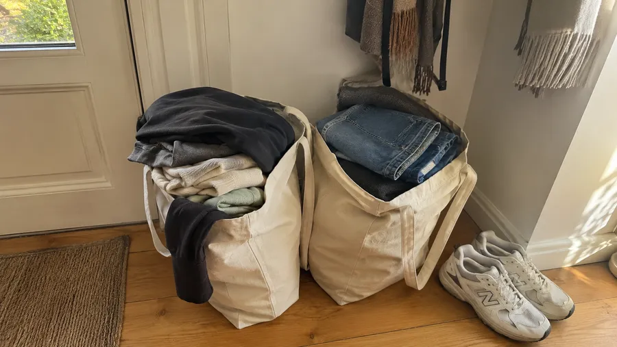 Zwei prall gefüllte Stofftaschen mit gefalteter Kleidung stehen an der Wohnungstür auf Holzboden