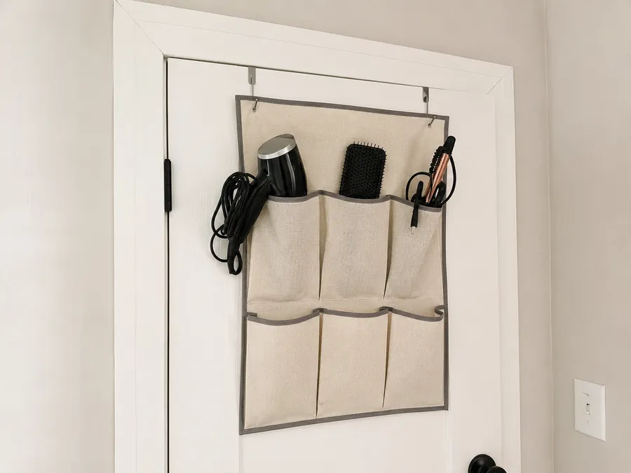 Türhänger-Organizer mit mehreren Stofftaschen an der Badezimmertür, darin Föhn, Bürste und Lockenstab