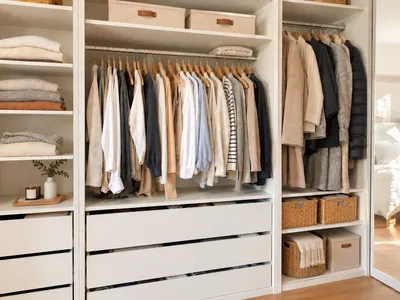 Vollständig organisierter begehbarer Kleiderschrank mit gehängter Kleidung, gefalteten Stapeln auf offenen Regalböden und geflochtenen Aufbewahrungsboxen